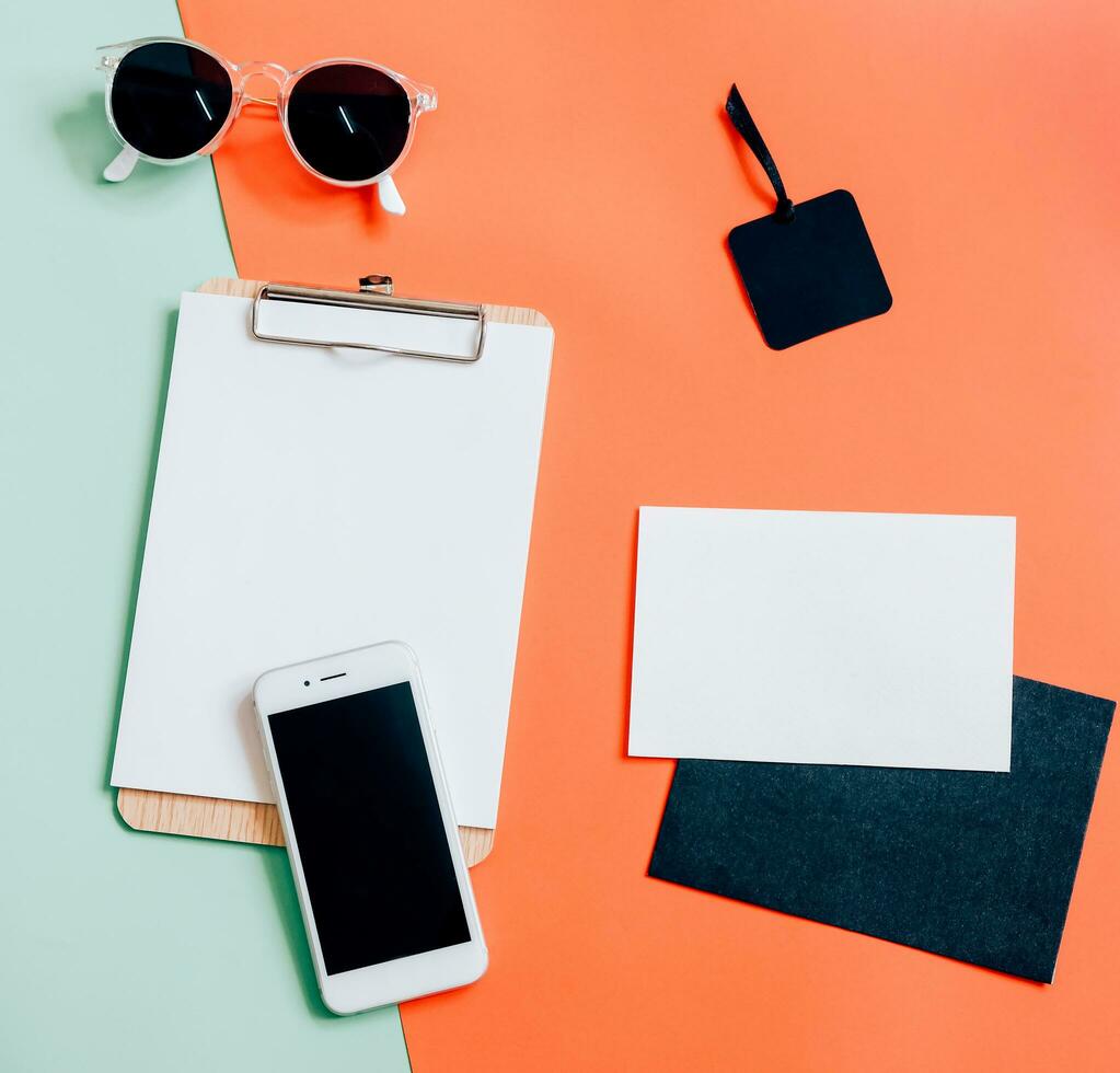 criativo plano deitar do área de trabalho escrivaninha com Smartphone, prancheta, envelope, tag e oculos de sol em mínimo cor fundo foto