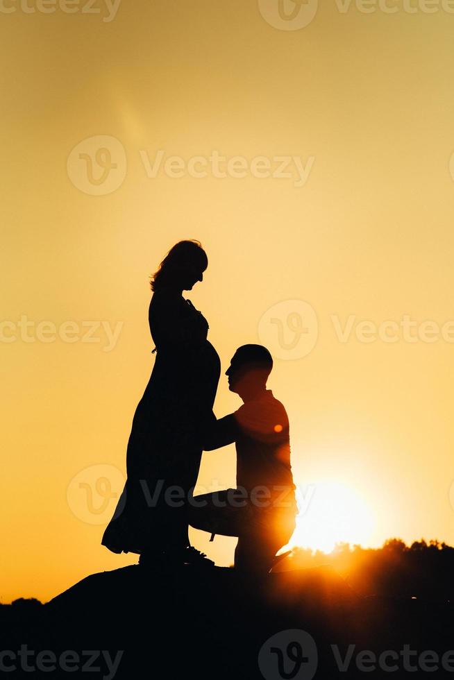silhuetas de uma jovem família feliz contra um pôr do sol laranja foto
