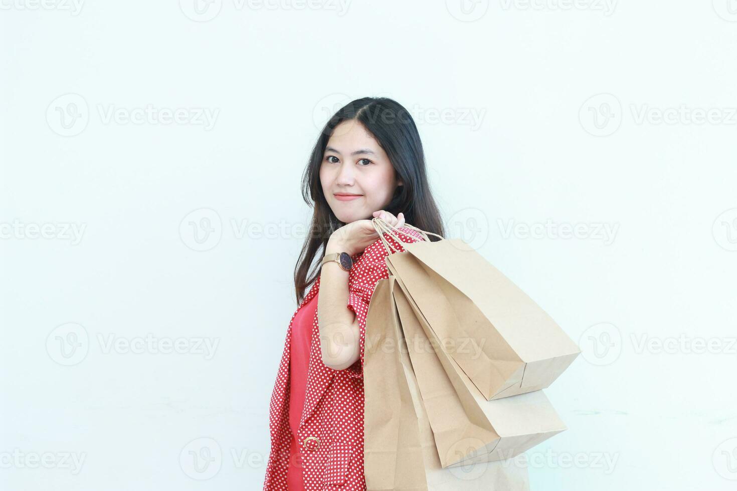 retrato do lindo ásia mulher vestindo vermelho equipamento gesticulando carregando grande quantidade do compras bolsas com feliz expressão foto