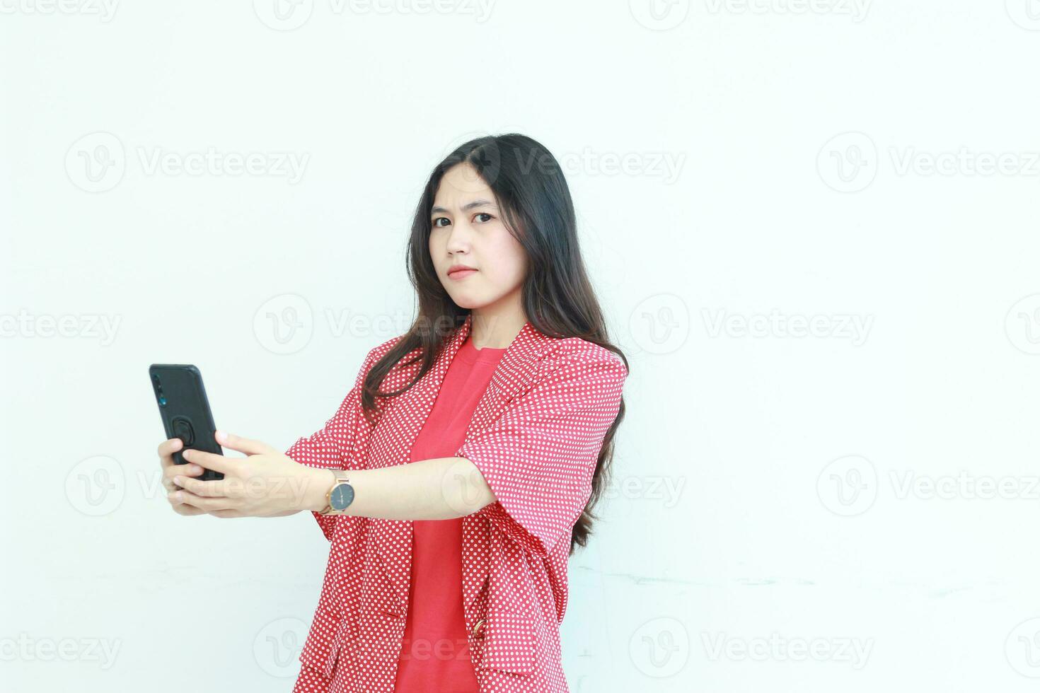 retrato do lindo ásia mulher vestindo vermelho equipamento segurando Móvel telefone com pensando expressão foto