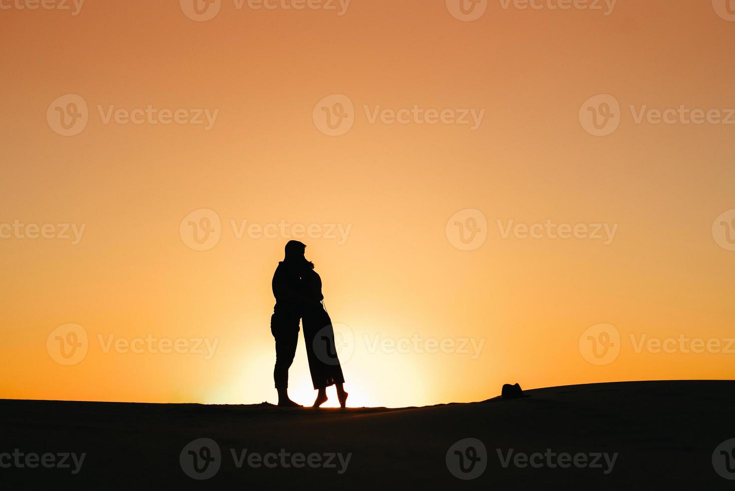 silhuetas de um jovem casal feliz em um fundo de pôr do sol laranja no deserto de areia foto