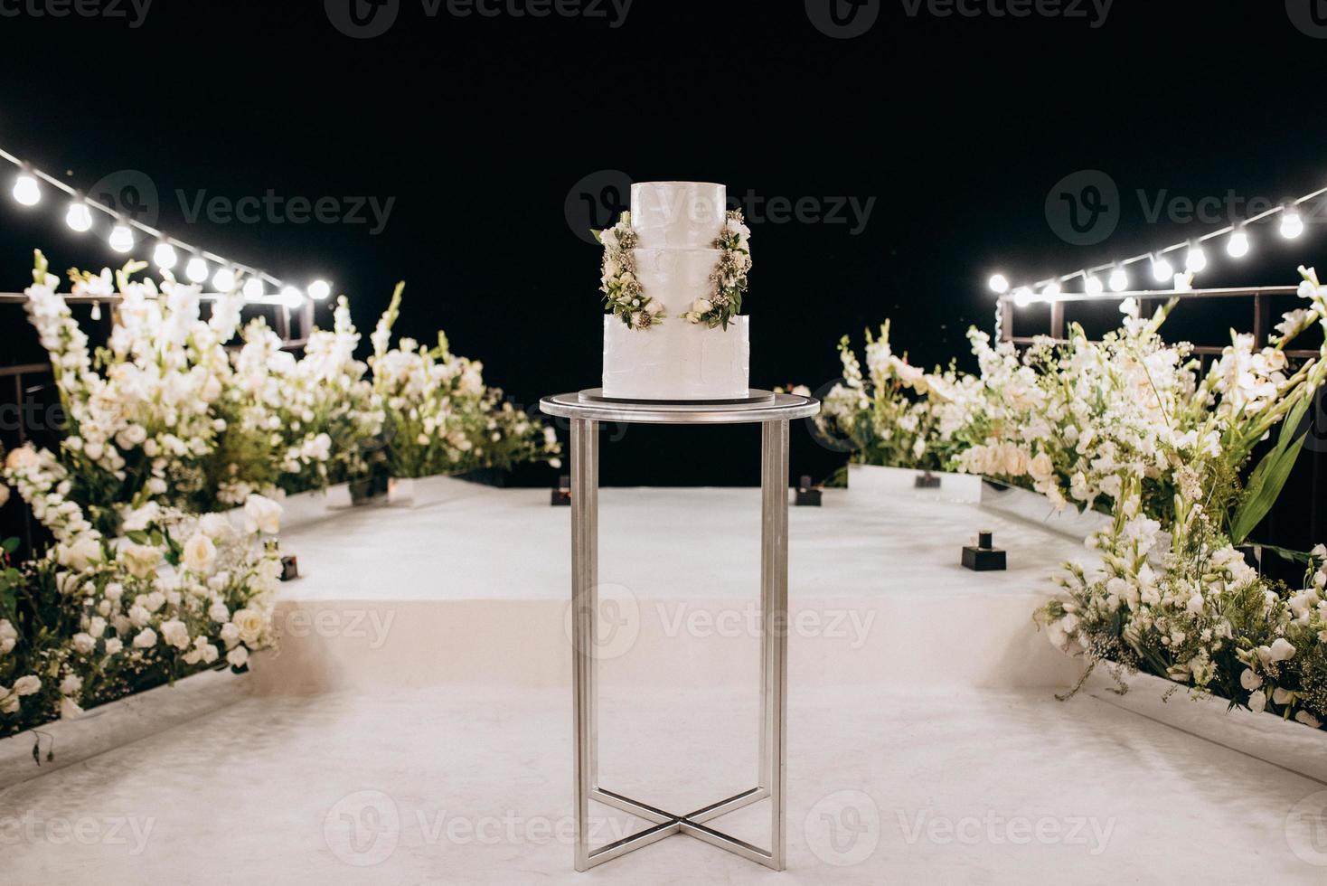 bolo branco de casamento em um alto suporte perto do pódio branco foto