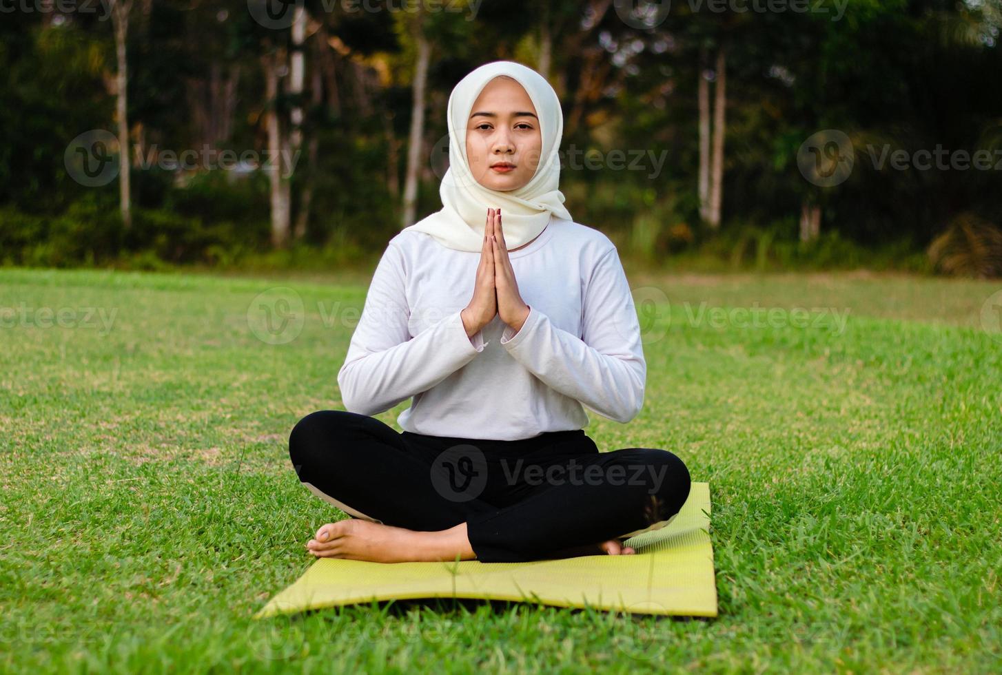 jovem muçulmana asiática sentada na grama, praticando meditação foto