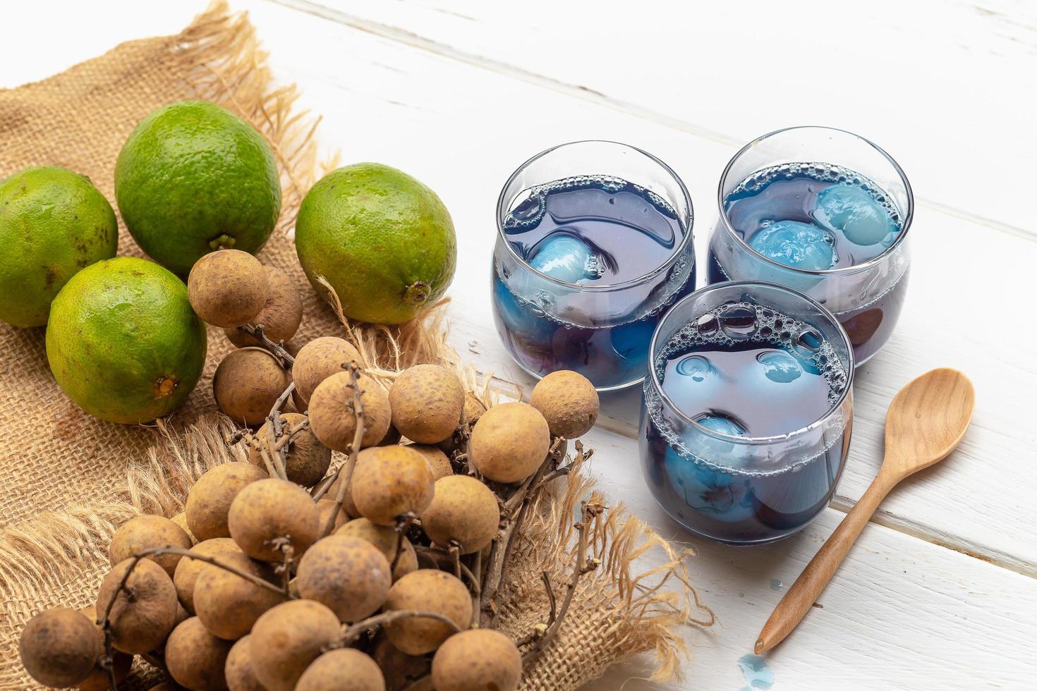 copo de suco de limão, flores de ervilha e longan na mesa de madeira branca foto