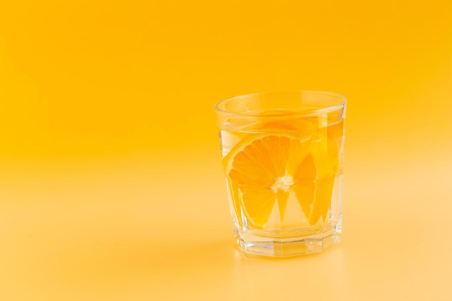 água de desintoxicação com laranja em um copo em um fundo laranja foto