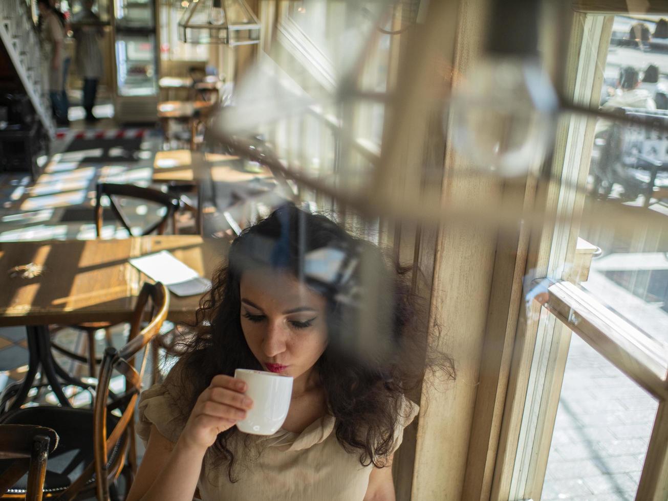 garota atraente com cabelo encaracolado sentada em um café à mesa e bebe café foto