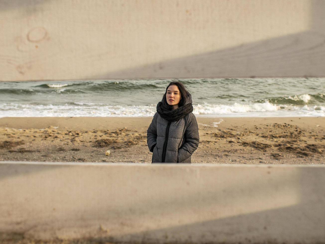 garota jovem e atraente em pé na areia, contra o fundo do mar. vista através de uma cerca de madeira. espiou a garota foto