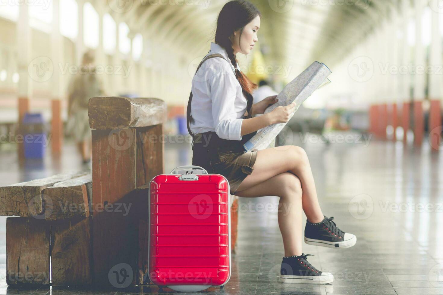 ásia mulher grávida sentar em a Banco Veja às a mapa com vermelho mala de viagem às estrada de ferro estação viagem, férias viagem conceito. foto