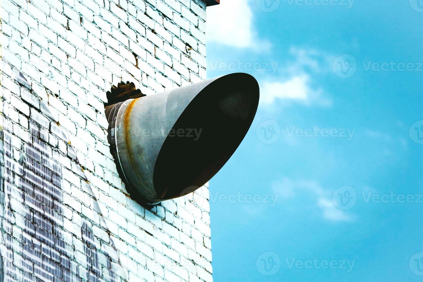 tubo de ar condicionado cortado na diagonal saindo da parede de tijolos brancos no céu azul com nuvens foto