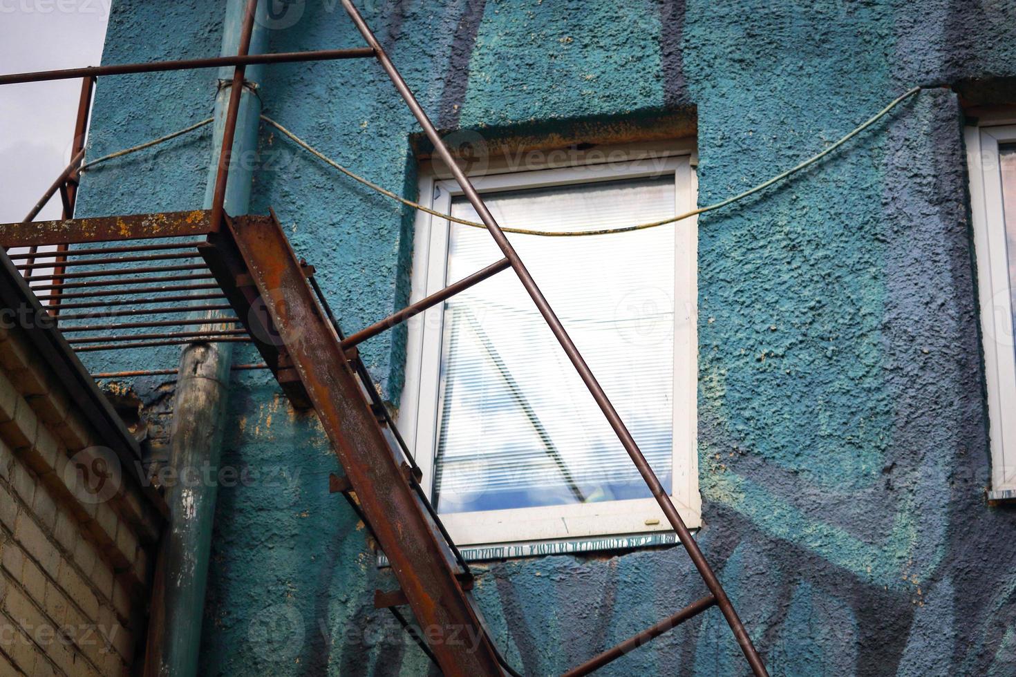 janela branca em parede texturizada azul com escadas de metal enferrujado embaixo foto