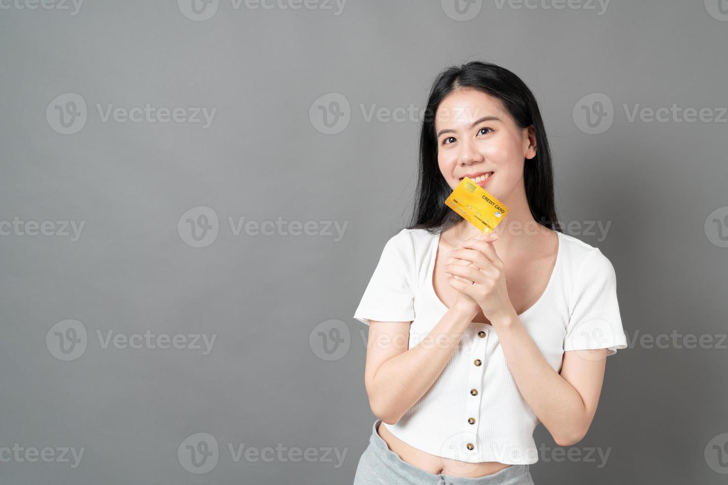 mulher asiática com cara feliz e apresentando cartão de crédito na mão, mostrando confiança e segurança para fazer o pagamento foto