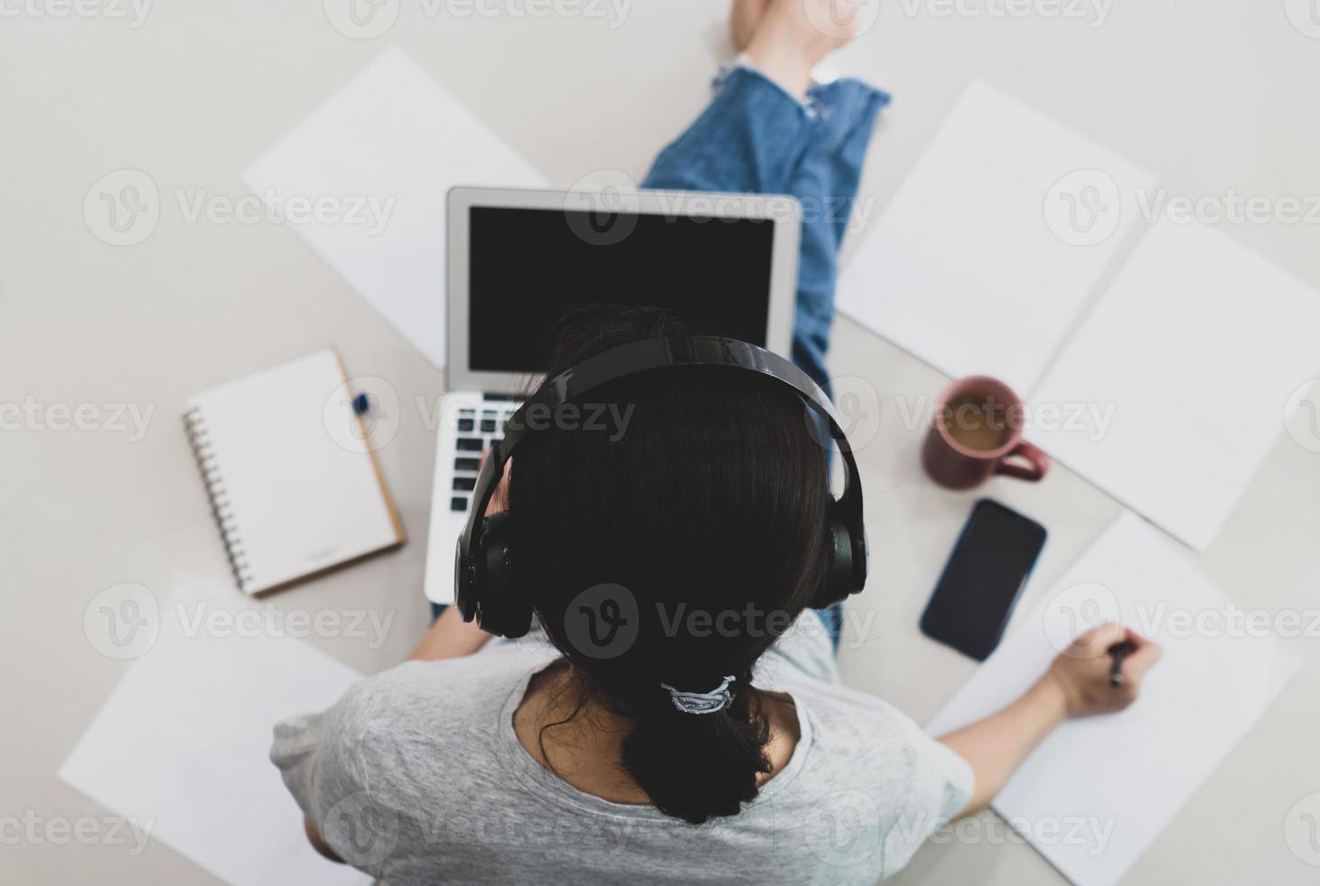 uma mulher asiática freelance usando o computador para trabalhar em casa na sala de estar pela manhã durante covid-19 ou pandemia de coronavírus. novo conceito normal e de tecnologia foto