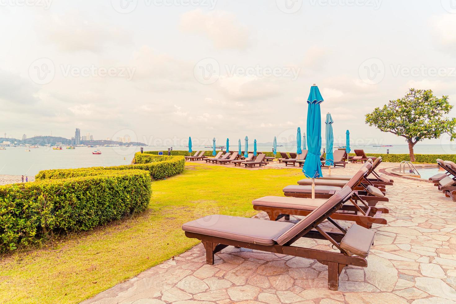 Piscina com cadeiras ou piscina com cama e guarda-sol ao redor da piscina com fundo de praia do mar em Pattaya, na Tailândia foto