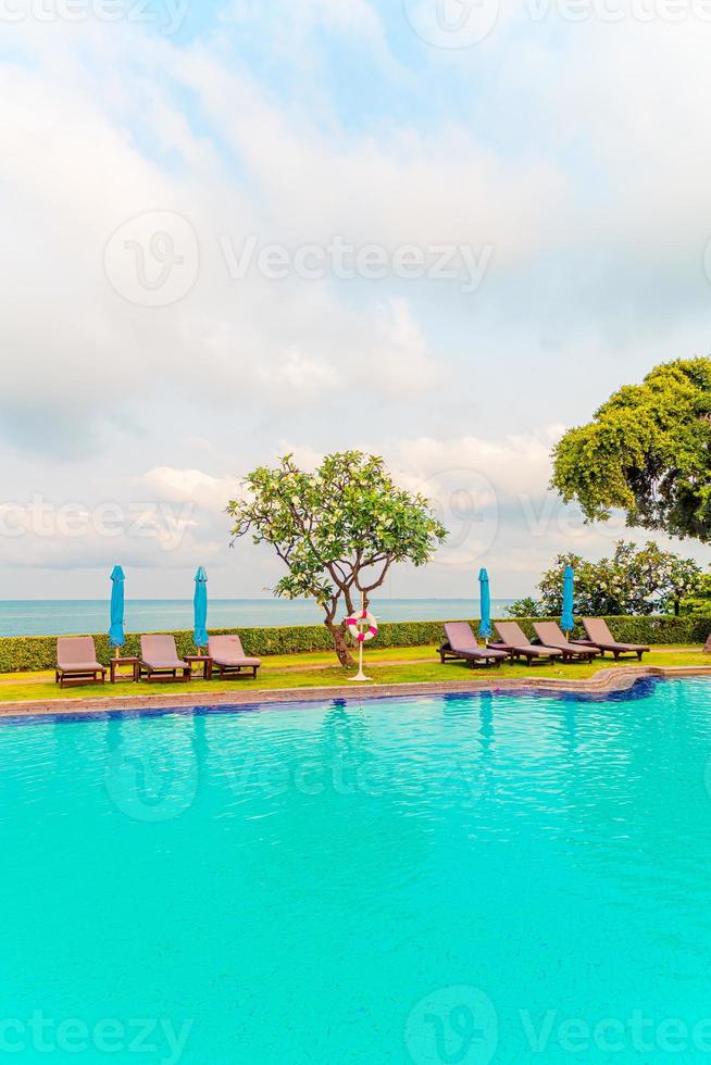 cadeira de piscina e guarda-sol ao redor da piscina com fundo do mar foto