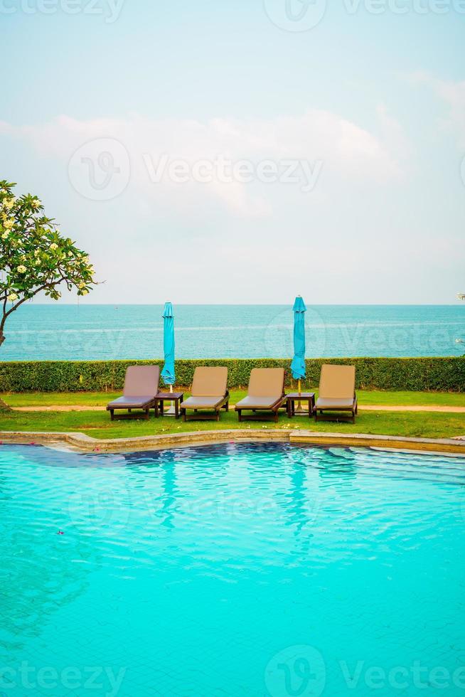 cadeira de piscina e guarda-sol ao redor da piscina com fundo do mar foto