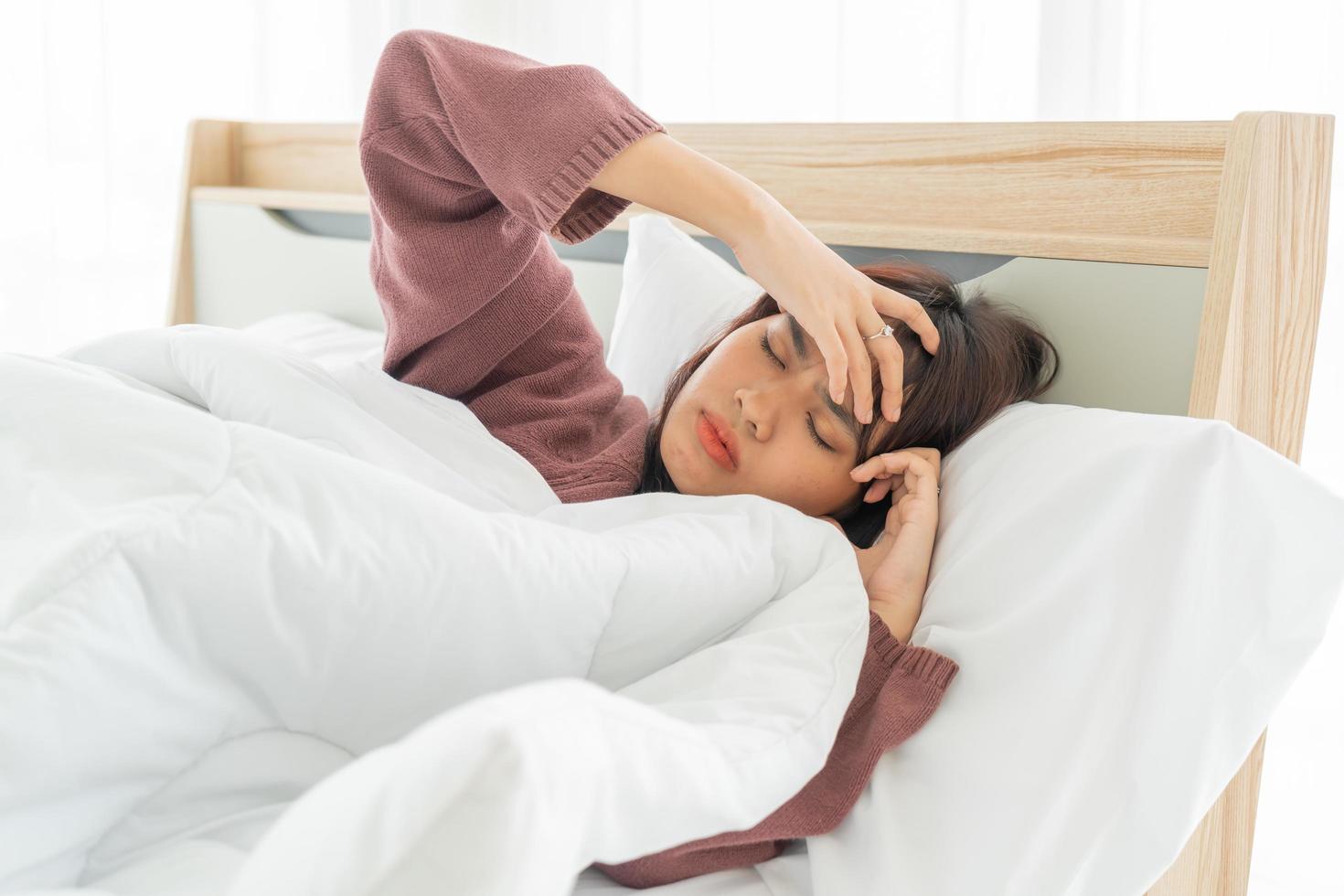 mulher asiática com dor de cabeça e dormindo na cama foto