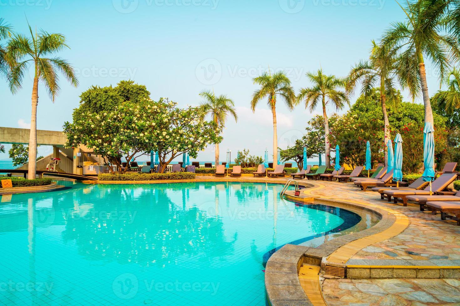 espreguiçadeiras e guarda-sóis ao redor da piscina com coqueiros - feriados e conceito de férias foto