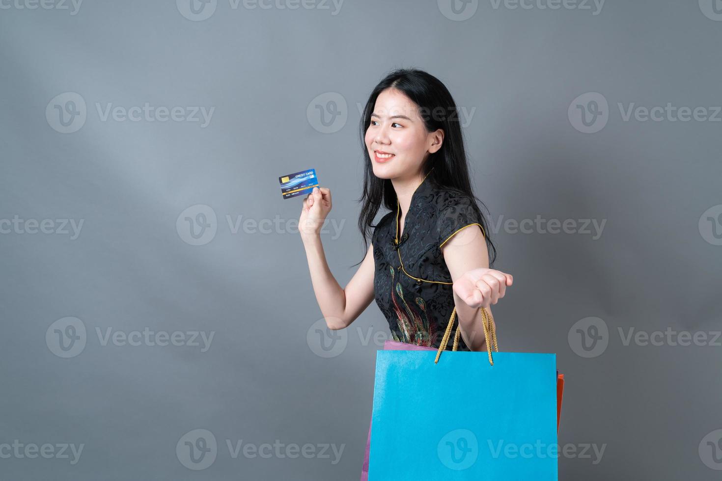 Mulher asiática usa vestido tradicional chinês com sacola de compras e cartão de crédito foto