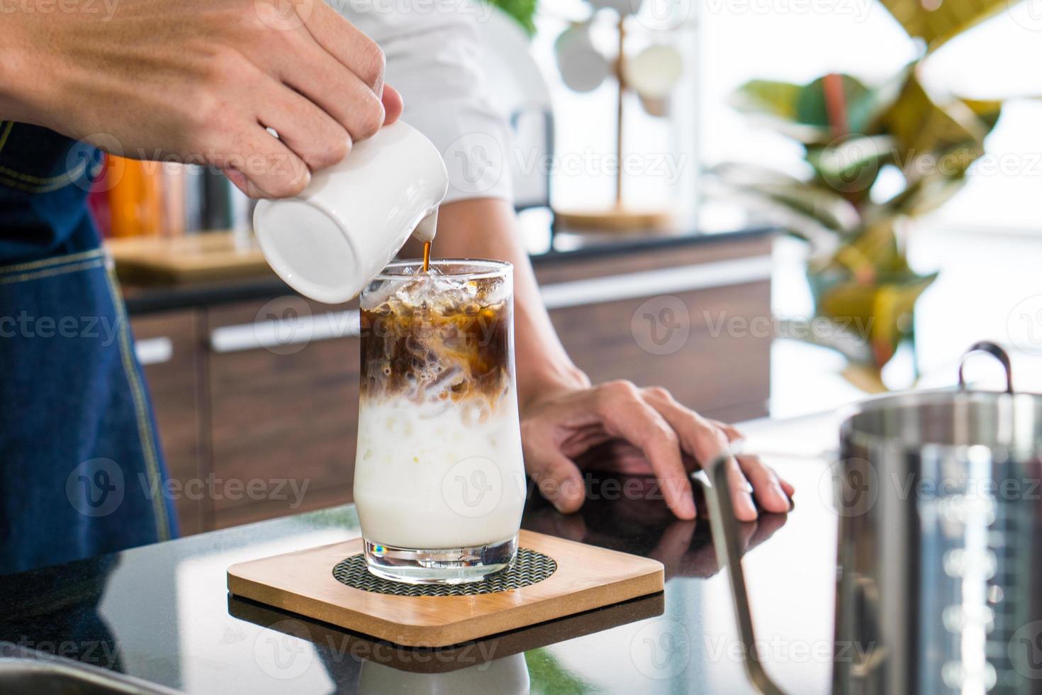 jovem servindo café em um copo que continha leite gelado. conceito de barista e cafeteria foto