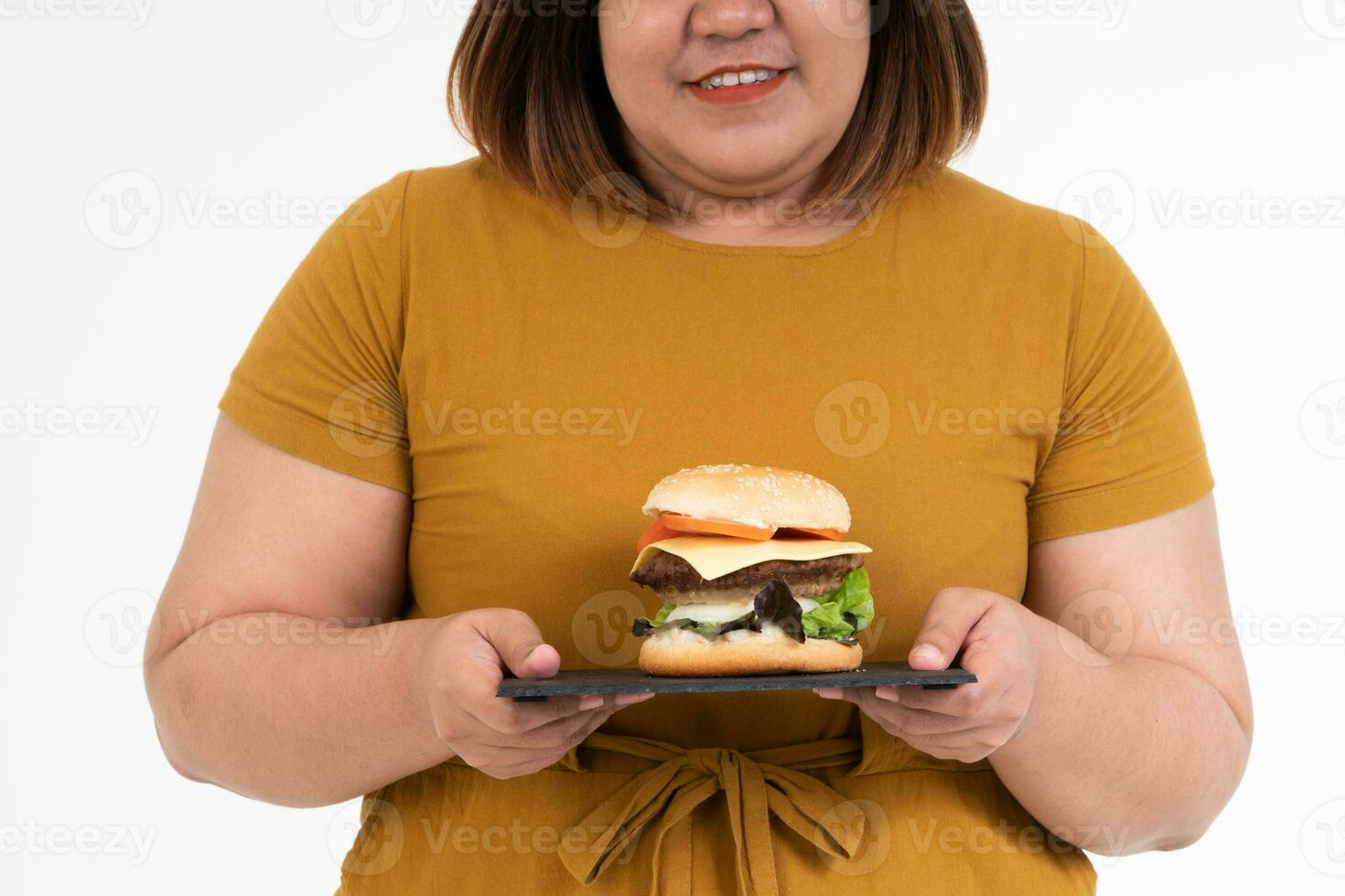 com fome excesso de peso jovem ásia mulher segurando Hamburger em isolado fundo, dela com fome todos Tempo e comer demais, gula e devoção comendo. dela estilo de vida é comendo velozes Comida todos tempo. pouco saudável conceito foto