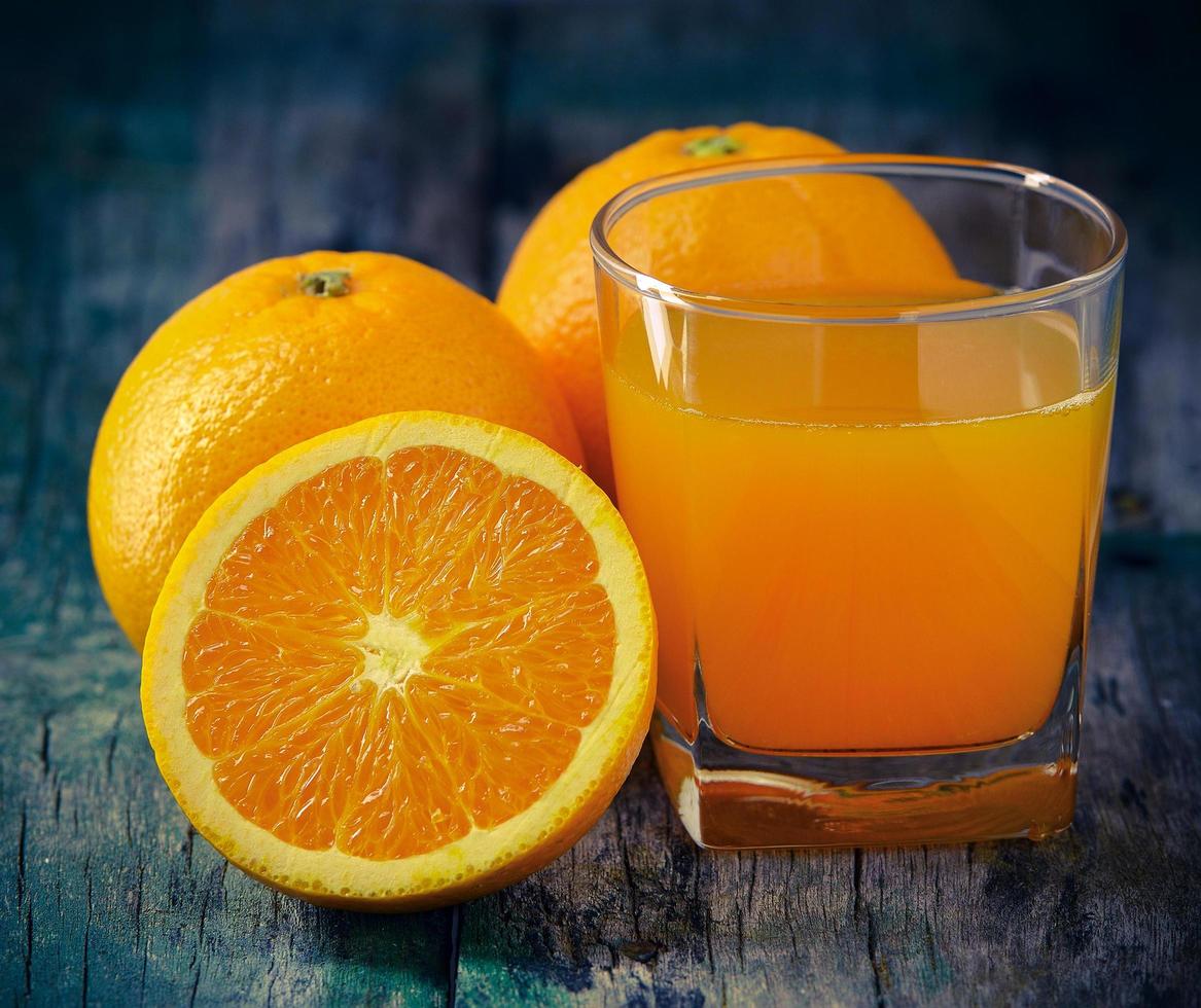 copo de suco de laranja e laranjas frescas na madeira foto