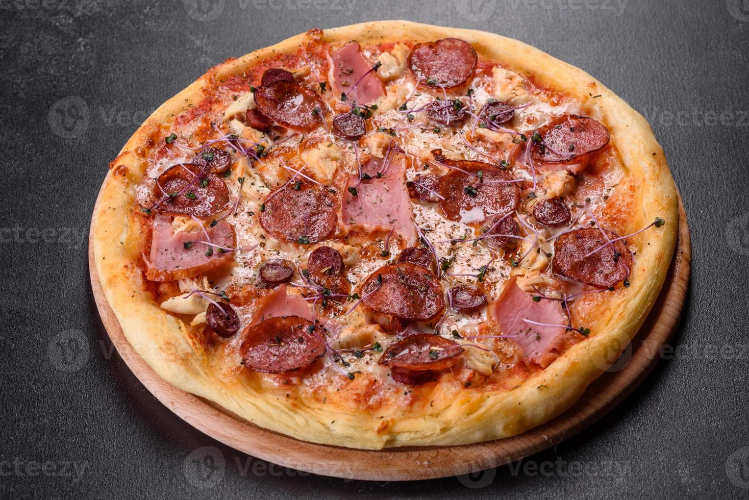 deliciosa pizza fresca de forno com tomate, salame e bacon em um fundo escuro de concreto foto