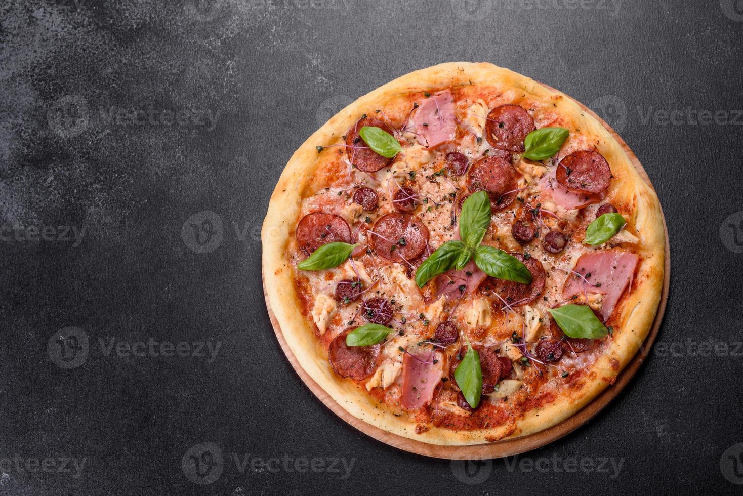 deliciosa pizza fresca de forno com tomate, salame e bacon em um fundo escuro de concreto foto