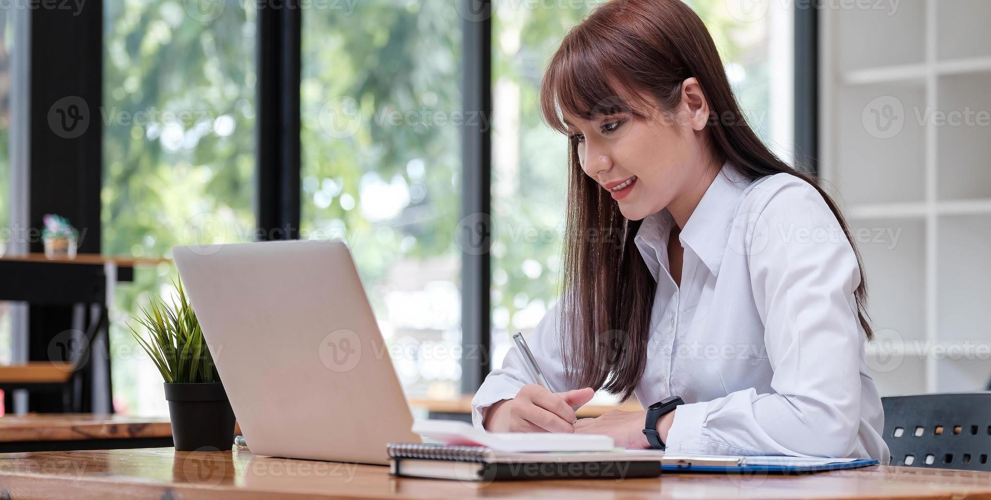 jovem empresária asiática sentada e feliz trabalhando com o laptop foto