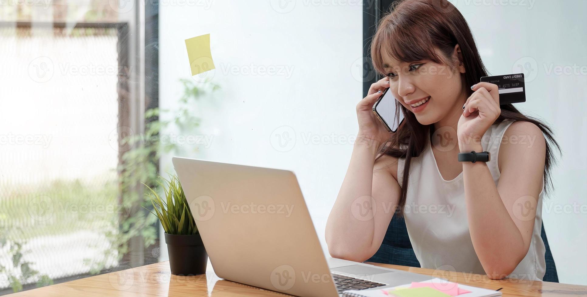 mulher sorridente, sentada no escritório, falando no celular foto