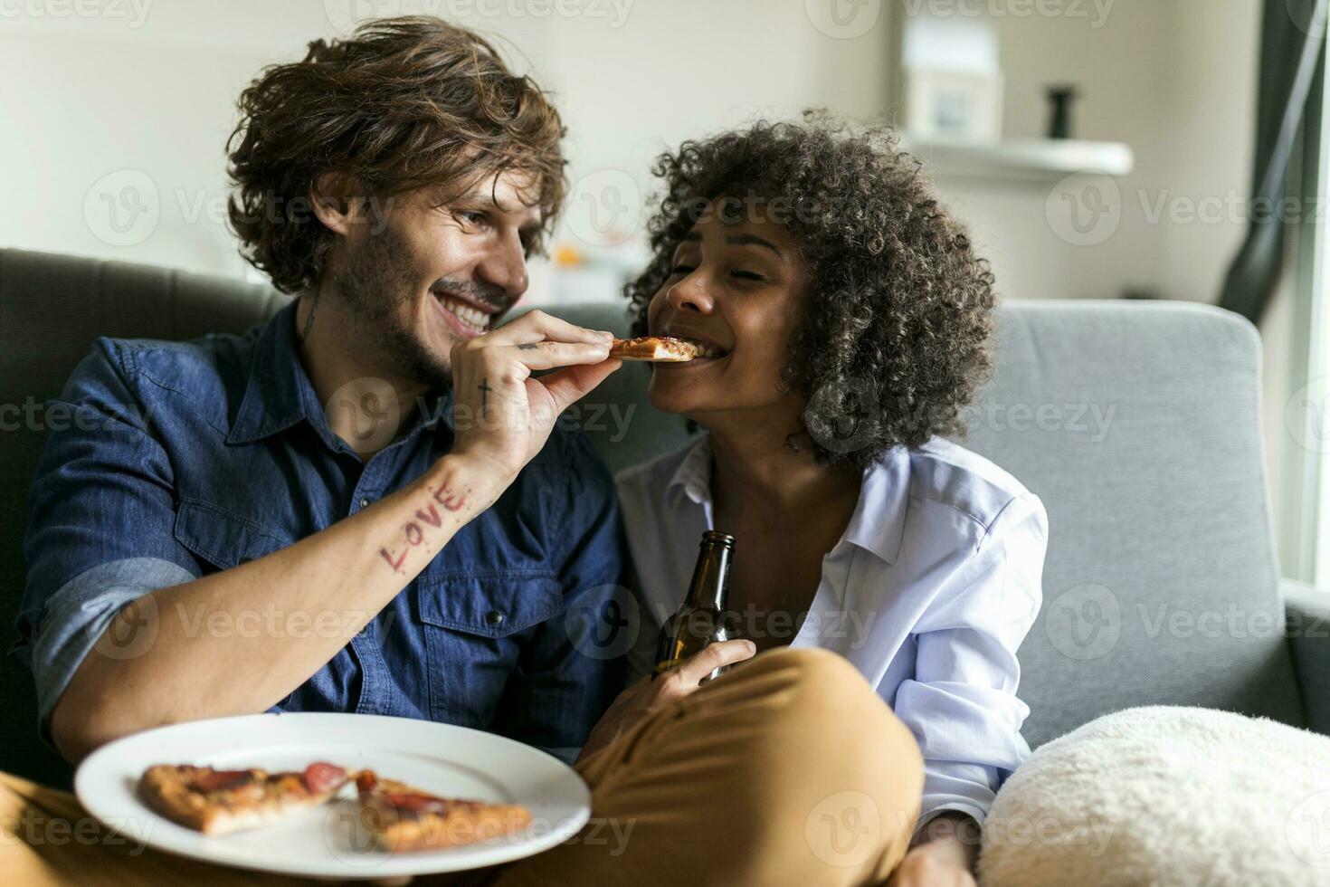 feliz casal sentado em sofá comendo pizza foto