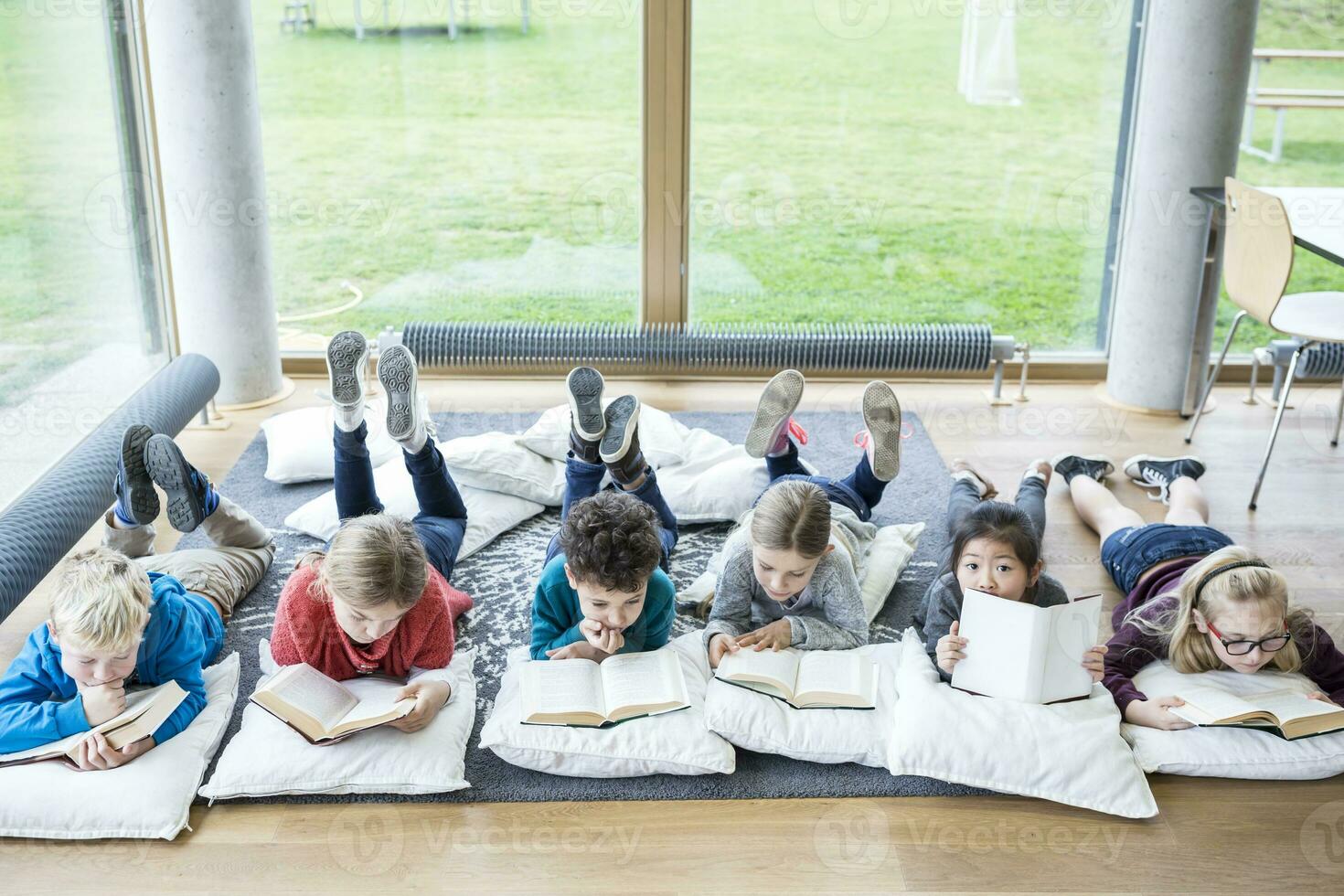 alunos deitado em a chão lendo livros dentro escola pausa quarto foto