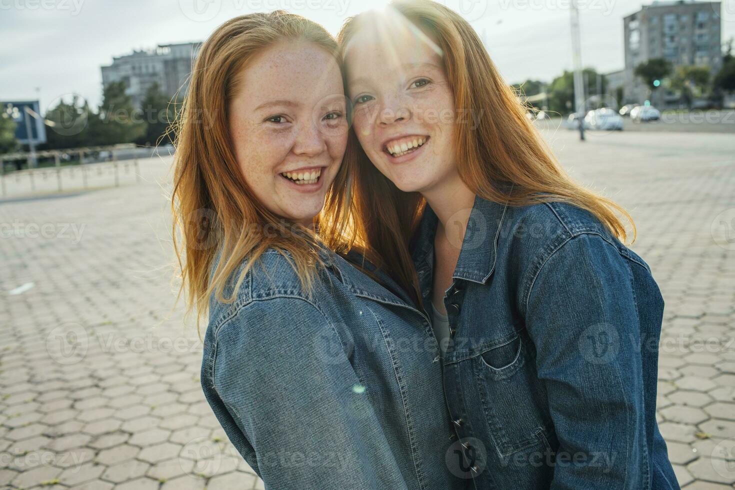 sorridente ruiva gêmeos dentro a cidade, luz solar foto
