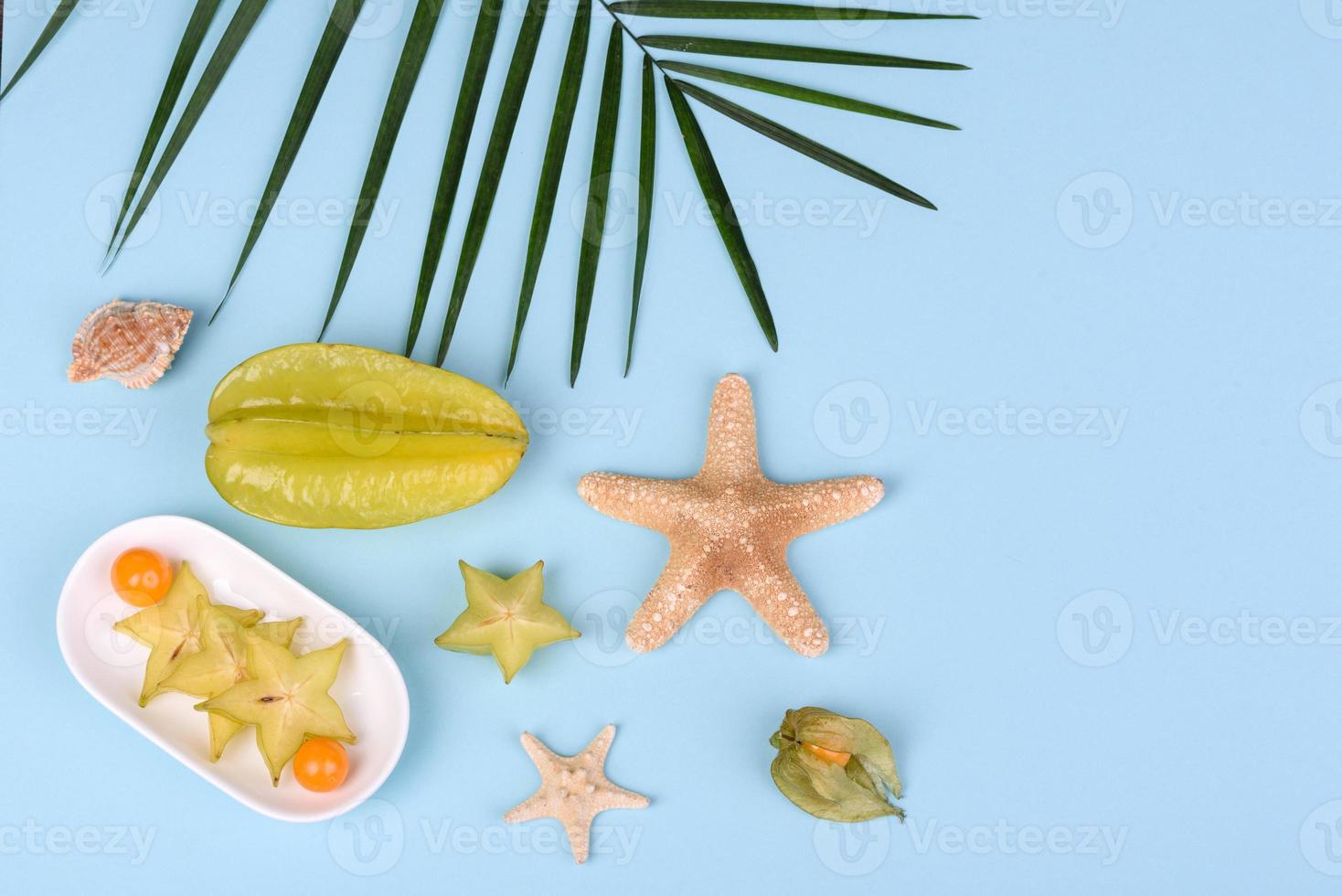 carambola de frutas, acessórios de praia e folhagem de planta tropical em papel colorido foto