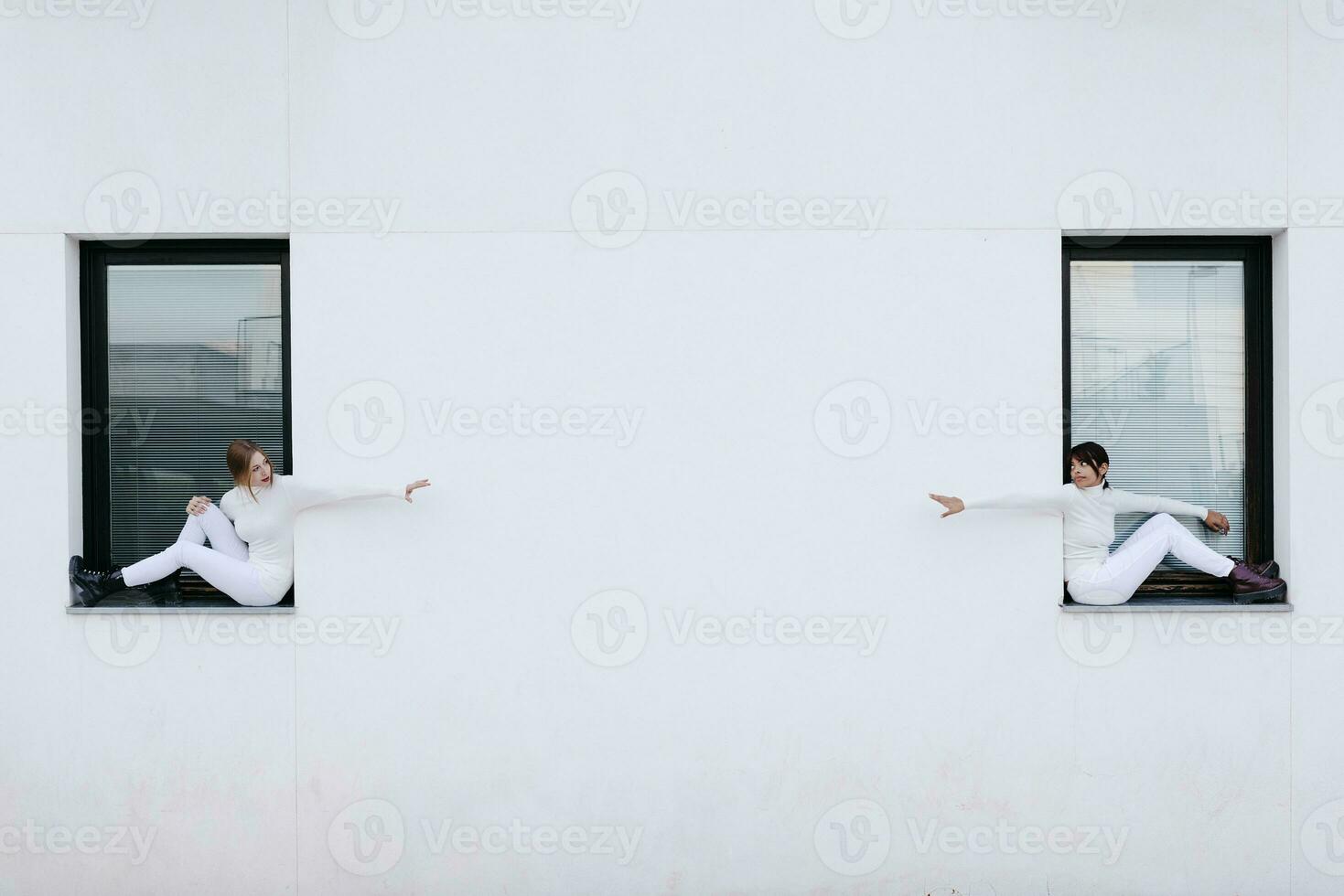 jovem mulheres sentado em janelas com braços estendido para cada de outros durante covid-19 foto