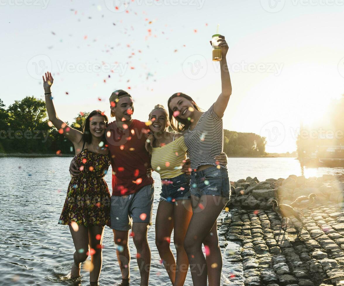 confete por aí grupo do feliz amigos tendo Diversão dentro uma rio às pôr do sol foto