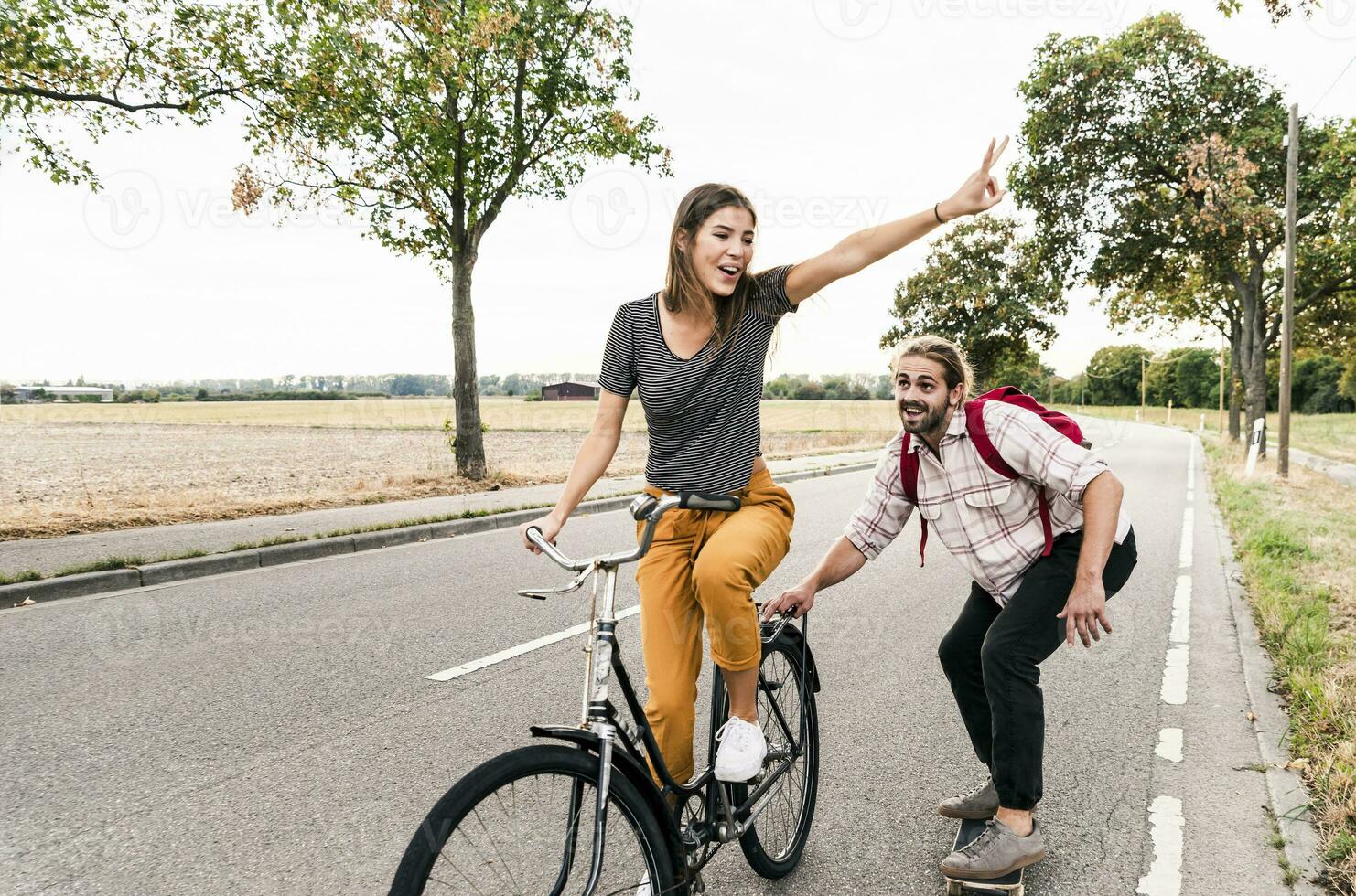feliz jovem casal com bicicleta e skate em país estrada foto