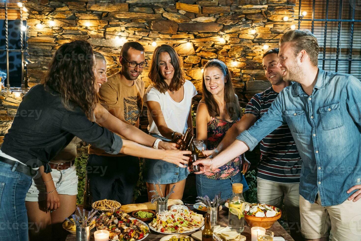 feliz amigos brindar com Cerveja garrafas durante a ao ar livre jantar foto