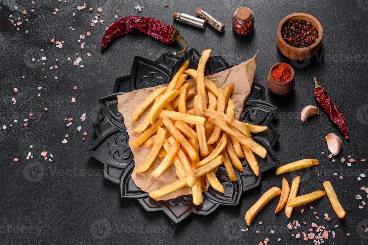 saborosas batatas fritas fritas com sal e especiarias em um fundo escuro foto