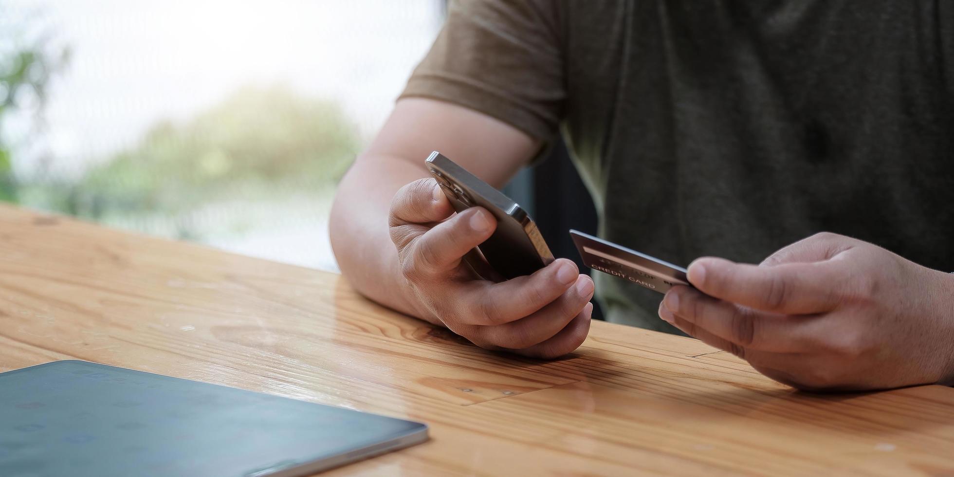 homem segurando cartão de crédito e usando smartphone em casa foto