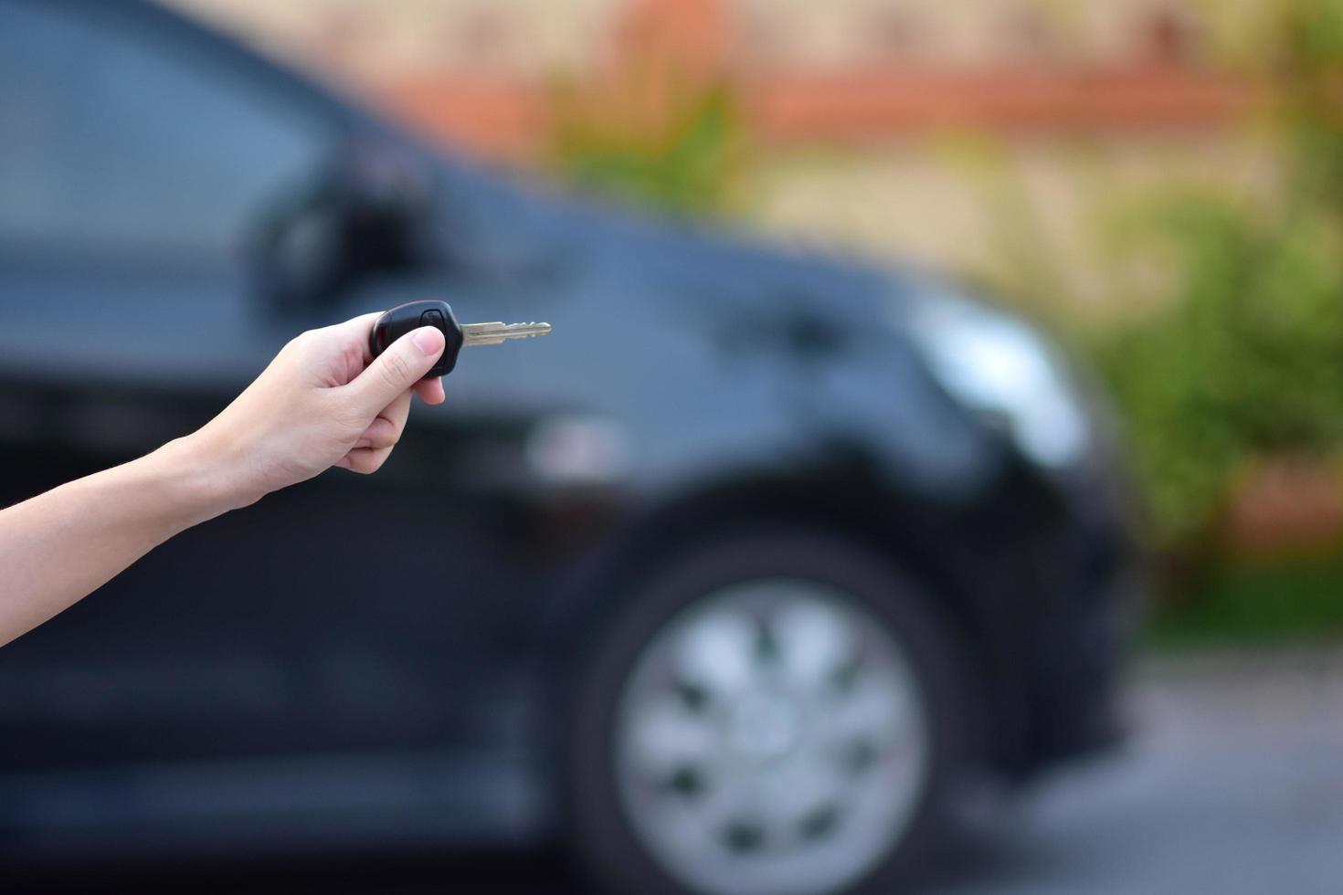 vendedor segurando a chave do carro e o carro estacionado no fundo foto