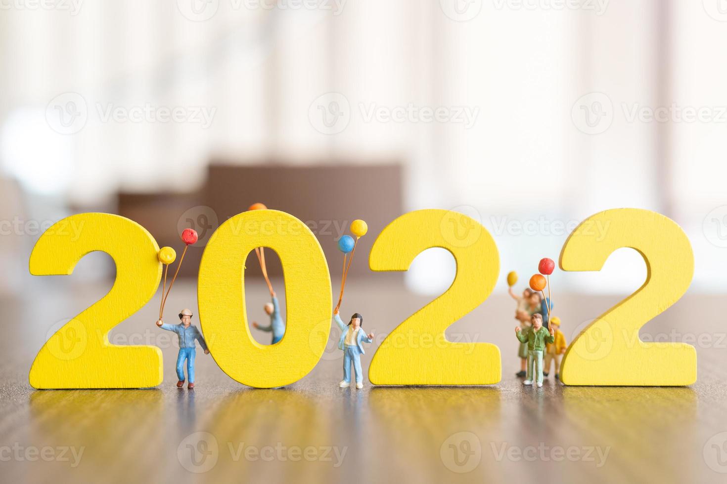 pessoas em miniatura família feliz segurando um balão no número branco 2022 foto