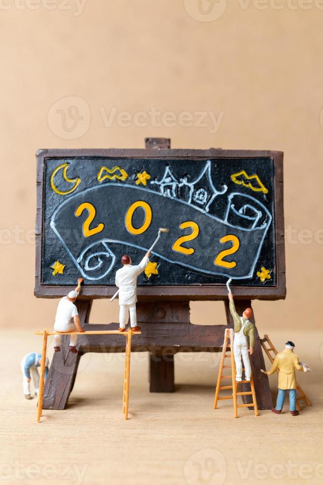 equipe de trabalho de pessoas em miniatura pintando o número 2022 no quadro negro foto