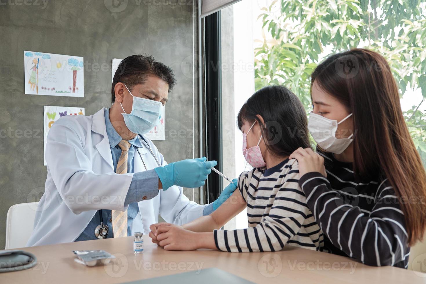 médico masculino vacinando menina asiática na clínica de pediatria. foto