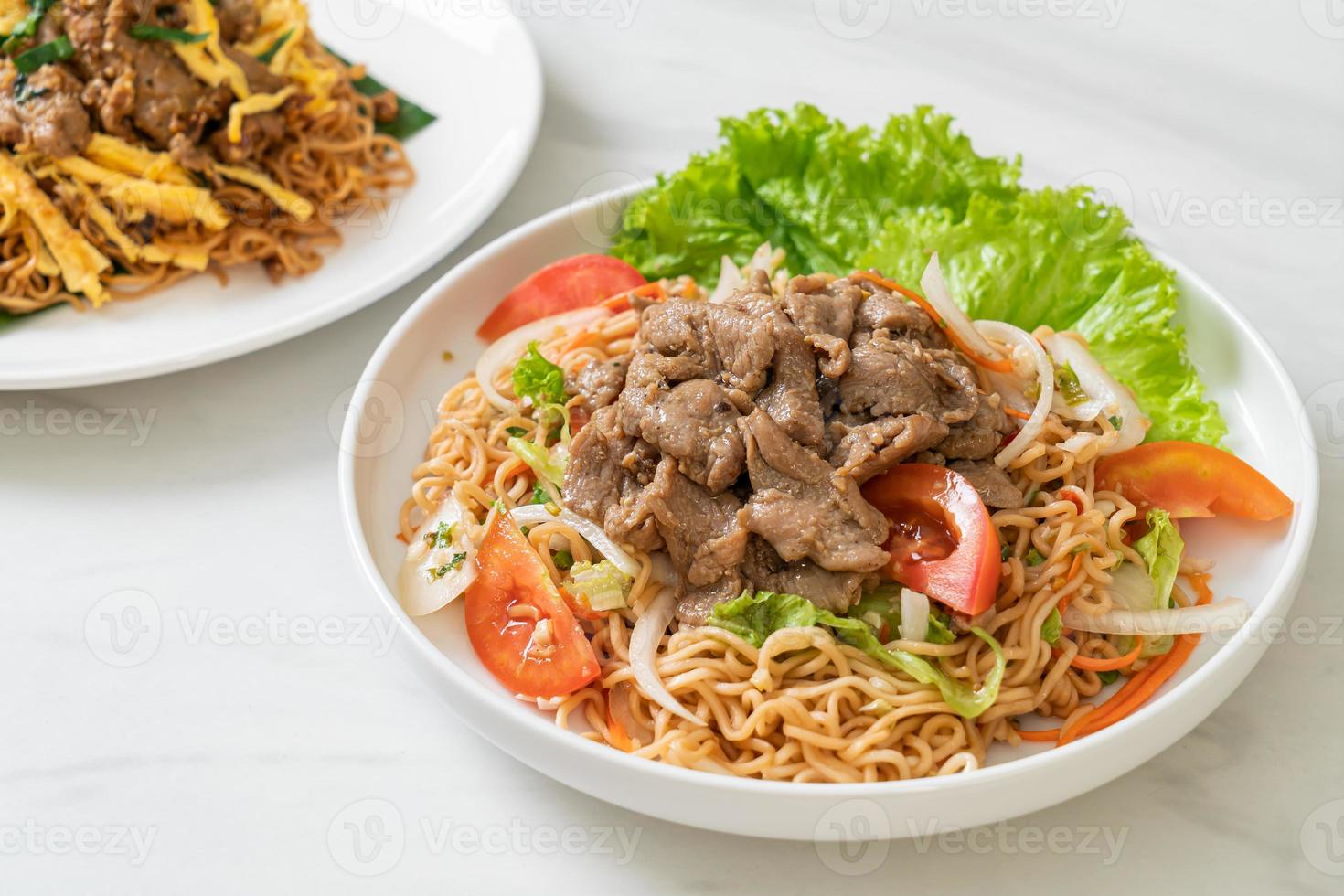 Salada picante de macarrão instantâneo com carne de porco no prato branco - comida asiática foto