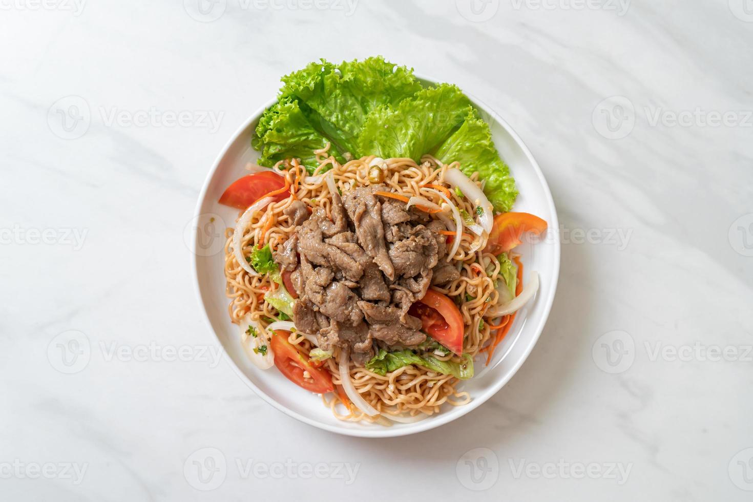 Salada picante de macarrão instantâneo com carne de porco no prato branco - comida asiática foto