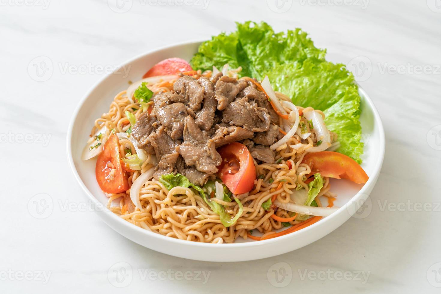 Salada picante de macarrão instantâneo com carne de porco no prato branco - comida asiática foto