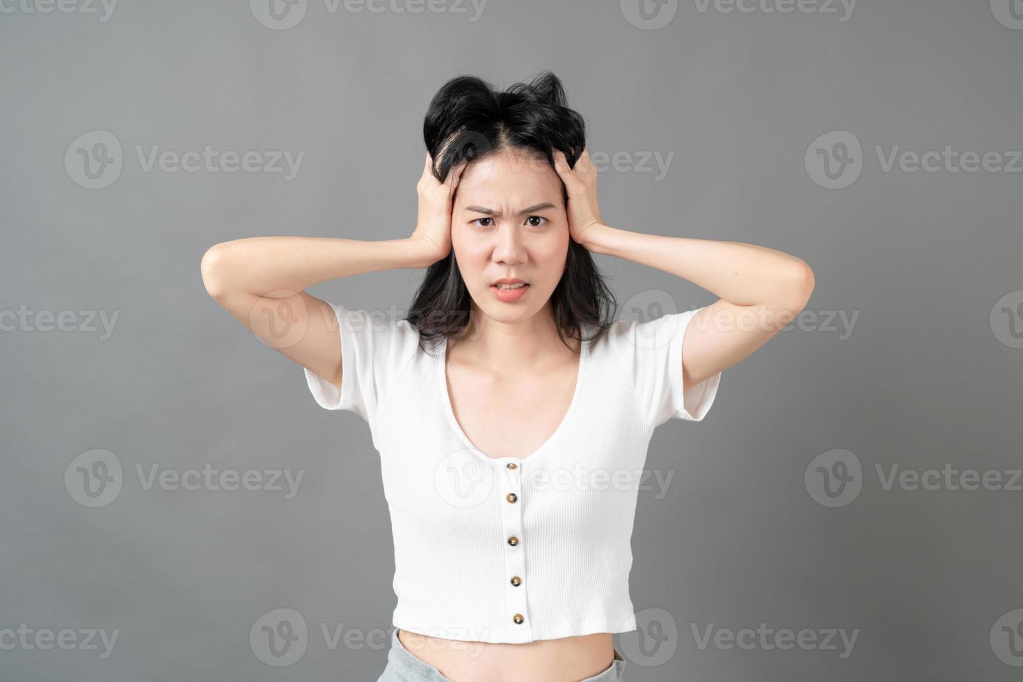 jovem mulher asiática com rosto sério e tenso em camisa branca em fundo cinza foto