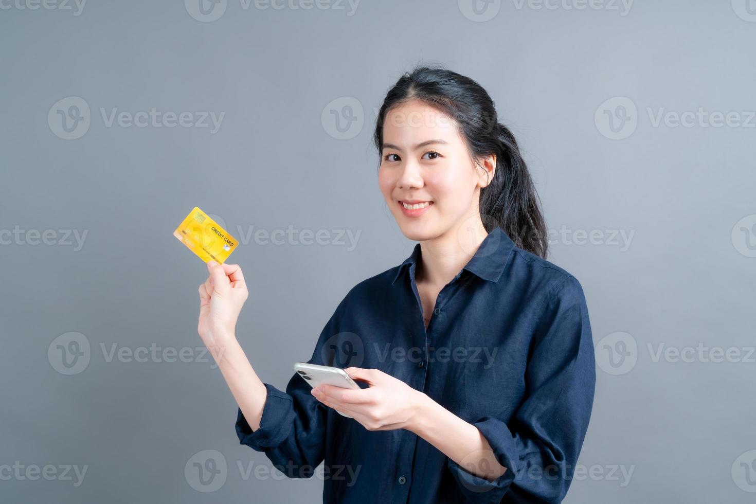 jovem asiática mostrando um cartão de crédito de plástico enquanto segura um telefone celular foto