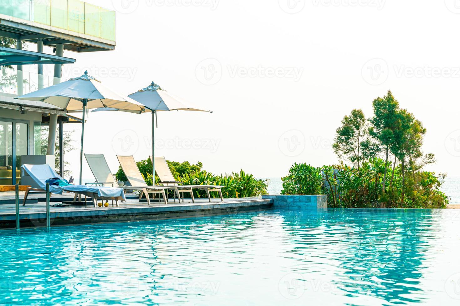 guarda-sol e cadeira ao redor da piscina com vista para o mar foto