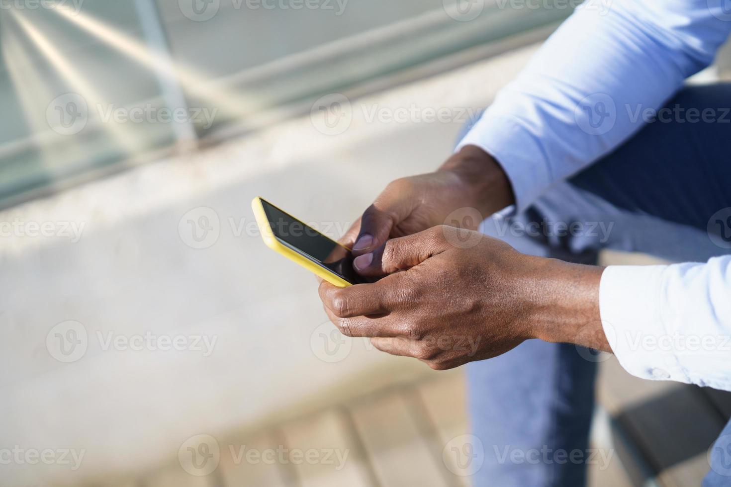 mãos de um homem negro irreconhecível, usando um smartphone. foto